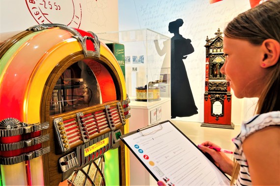 Ein Mädchen im Profil blickt auf die 40er-Jahre Jukebox Wurlitzer 1015 und hält einen Quizbogen und Stift in den Händen.